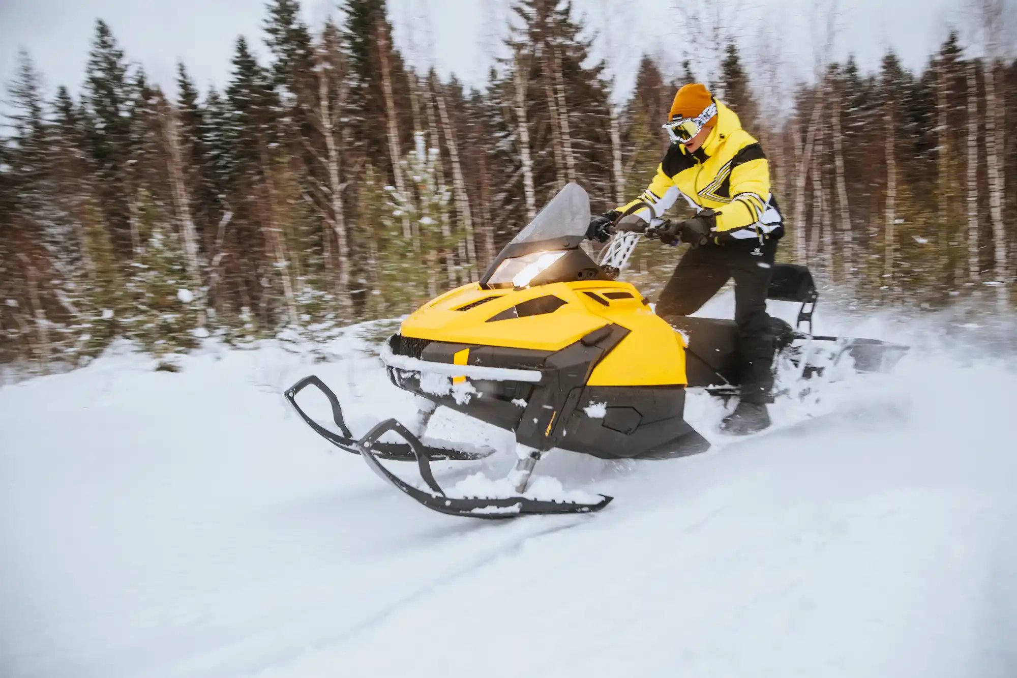 A-man-rides-a-yellow-snowmobile-through-a-winter